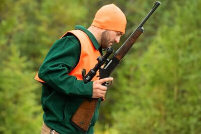 Hunter wearing blaze orange and carrying a Henry Long Ranger Big Woods Carbine while moving through dense timber during a whitetail hunt.