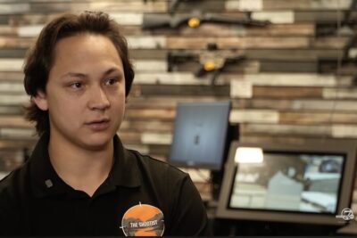 An employee at The Shootist gun store in Englewood, Colorado, discusses the impact of Colorado's new SB 25-003 semiautomatic firearm law as rifles are displayed behind him.