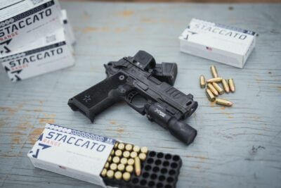 Staccato 2011 pistol with optic and weapon light surrounded by ammunition at a shooting range