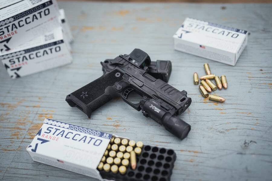 Staccato 2011 pistol with optic and weapon light surrounded by ammunition at a shooting range