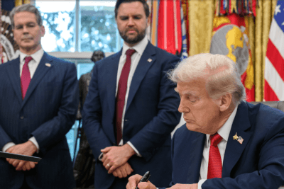 President Donald Trump signs a document at the White House as Vice President JD Vance and Treasury Secretary Scott Bessent look on.